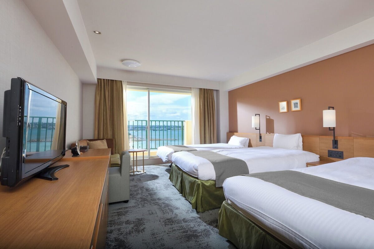 Une chambre d’hôtel avec deux lits, un bureau, une télévision et un balcon donnant sur l’eau.