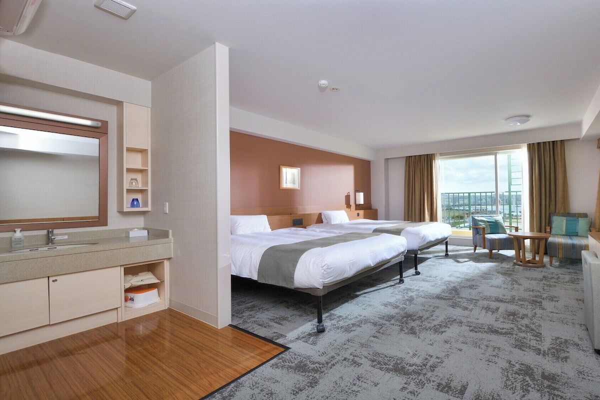 Une chambre d’hôtel avec un grand lit, un bureau avec un ordinateur, une télévision et un balcon offrant une vue sur la ville.