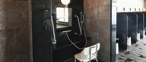 A modern restroom with a black wall, a mirror, a shower, and a white chair.