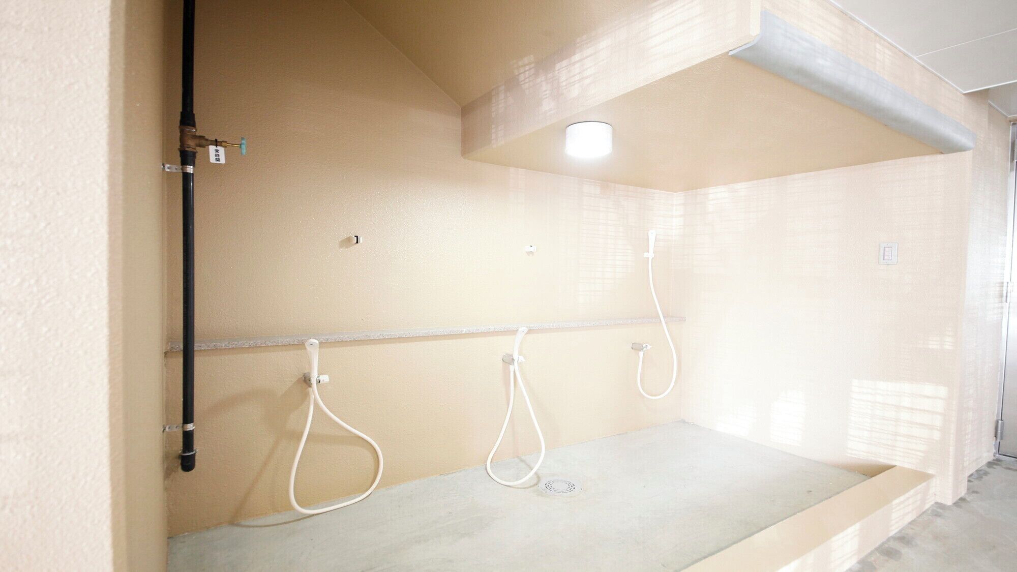 A bathroom with three white showerheads, a light fixture, and a visible water pipe.