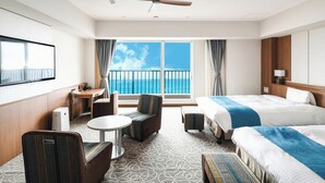 Een hotelkamer met een bed, een bureau, een stoel, een tafeltje en een balkon met uitzicht op zee.
