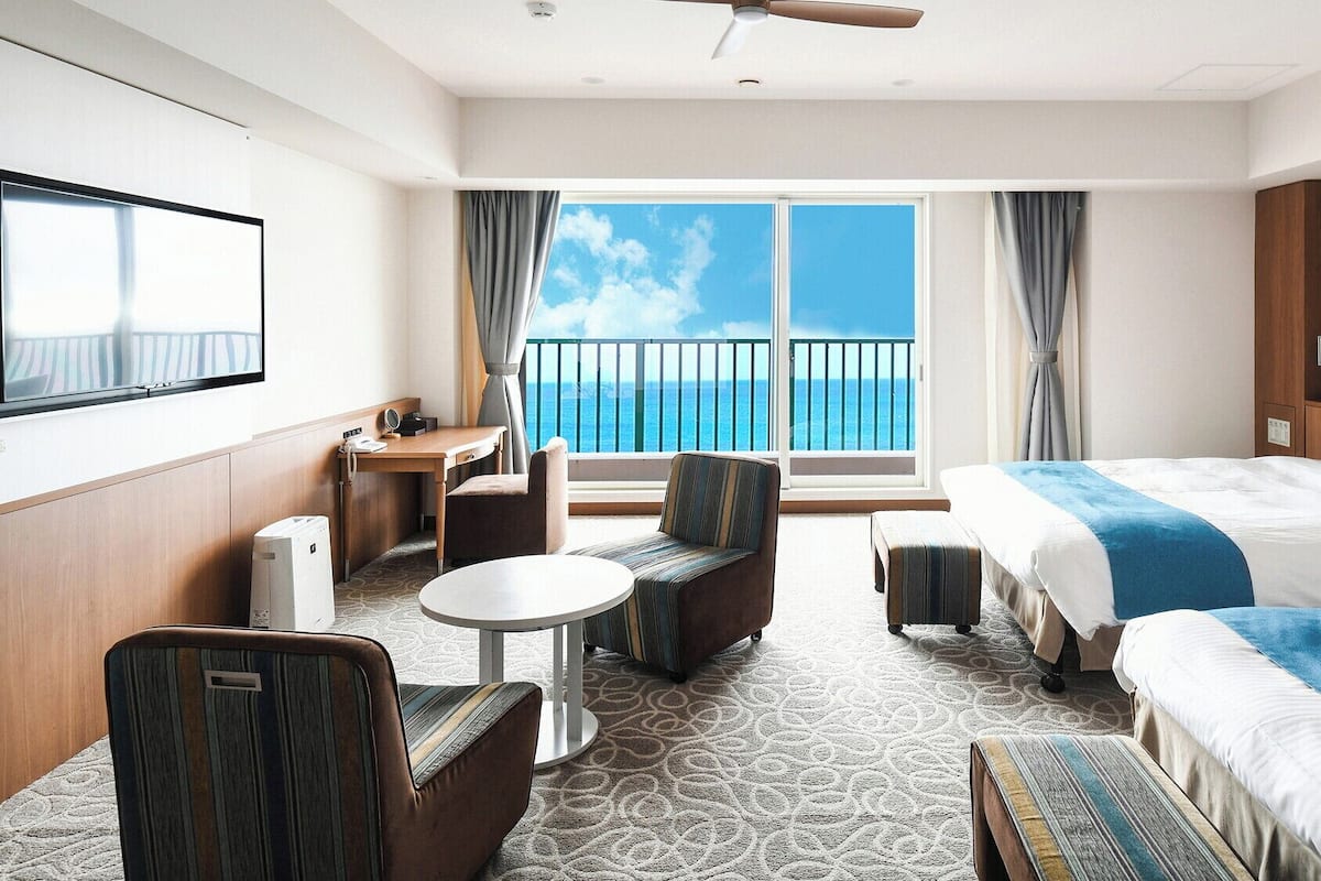 Une chambre d’hôtel comprenant un lit, un bureau, une chaise, une petite table et un balcon avec vue sur la mer.