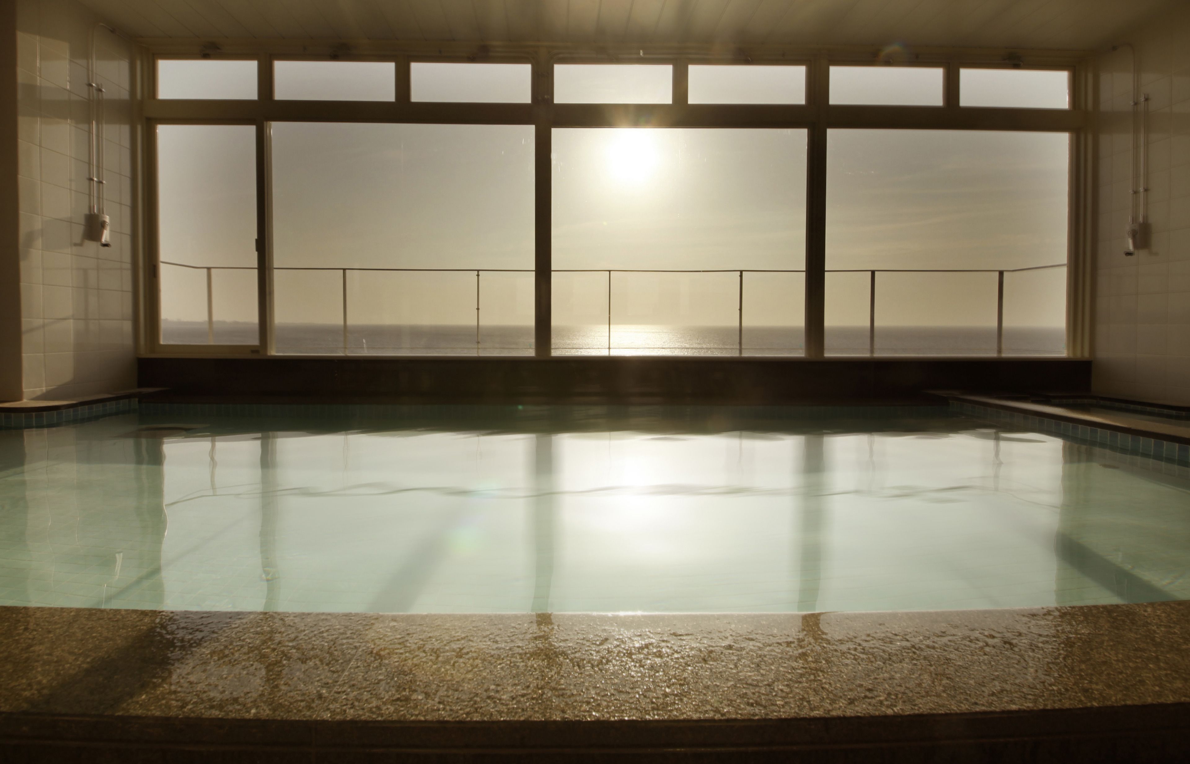 An indoor swimming pool with a view of the sea through large windows.
