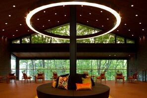 Un hall d’entrée spacieux avec un espace salon circulaire, de grandes fenêtres donnant sur la verdure et un luminaire moderne au plafond.