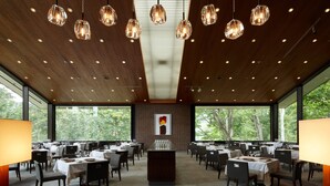 Un vaste espace dédié à la salle à manger, avec de nombreuses tables, des luminaires suspendus et de grandes fenêtres offrant une vue sur l’extérieur.