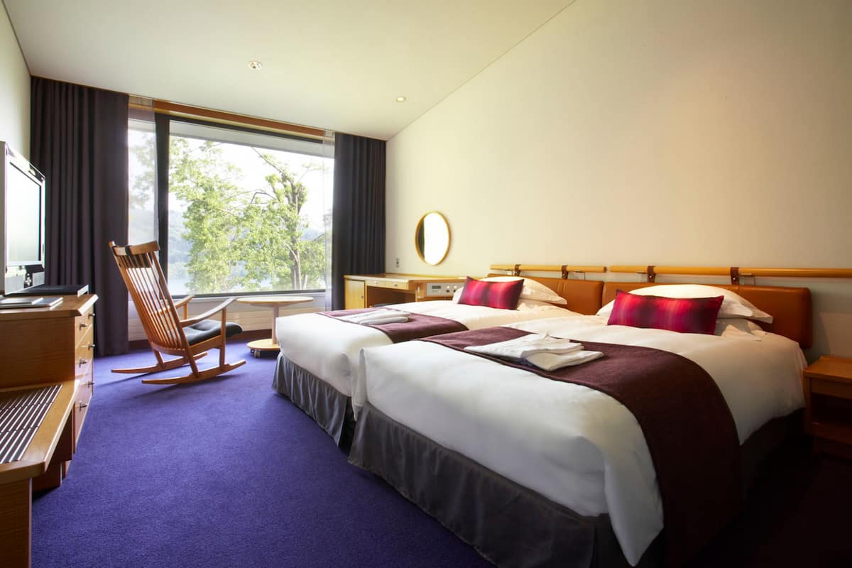 Een hotelkamer met twee bedden, een bureau, een stoel en een groot raam.