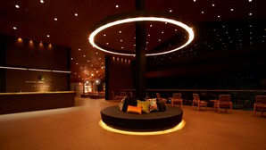 Un hall d’hôtel doté d’un espace salon circulaire, d’un comptoir d’accueil et d’un grand élément décoratif lumineux au plafond.