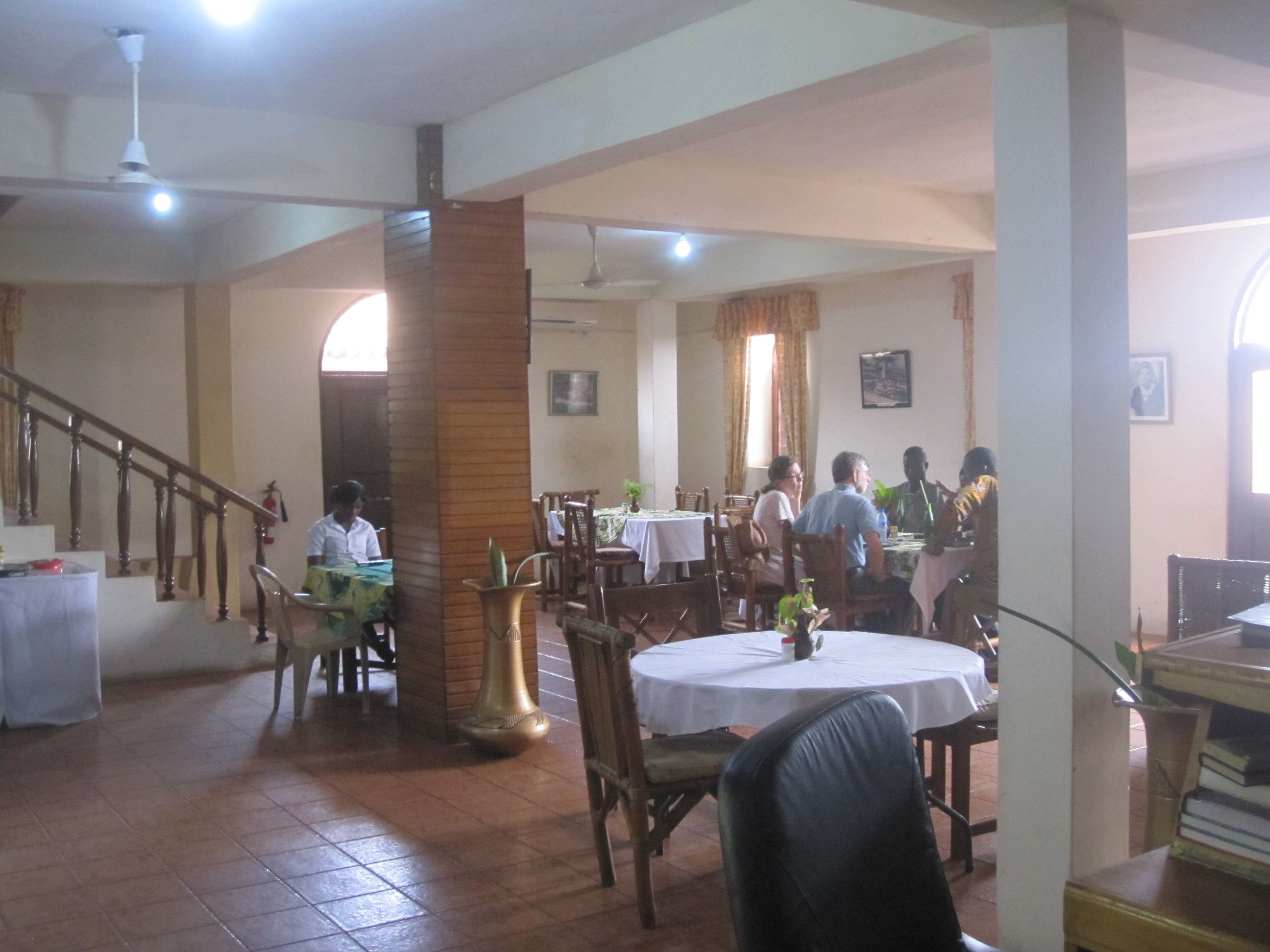 A restaurant with multiple tables and chairs, a staircase, and a few people dining.