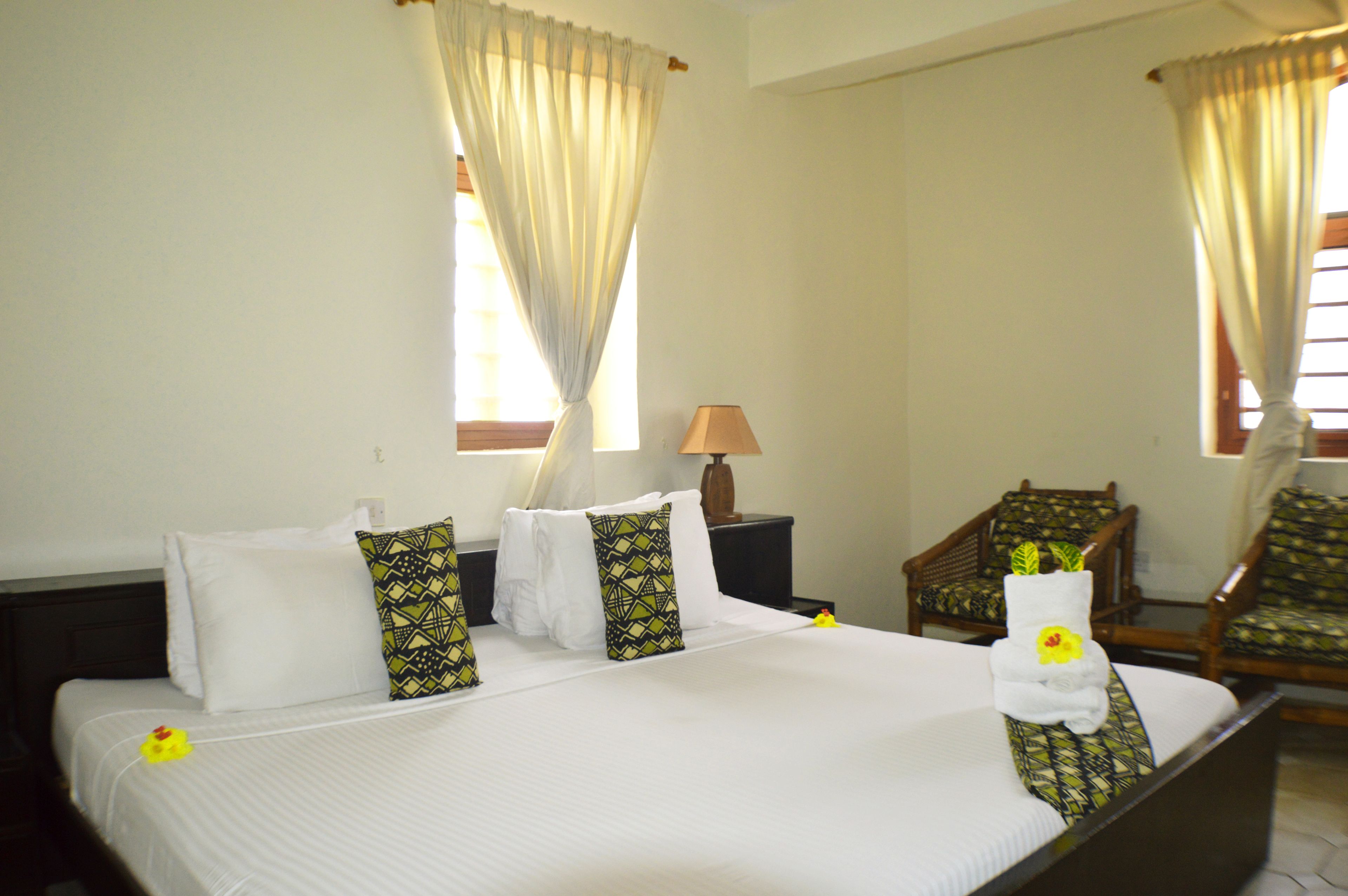 A hotel room with a neatly made bed, a chair, a lamp, and curtains.