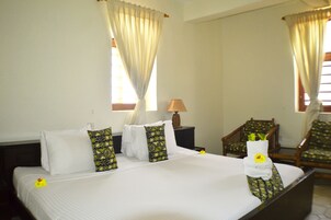Una habitación de hotel con una cama bien hecha, una silla, una lámpara y cortinas.