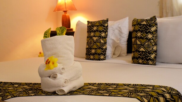 A neatly made bed with a rolled towel and a decorative flower, patterned pillows, and a bedside lamp.