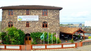 A stone building with a sign for Coconut Grove Bridge House, featuring a restaurant, tea & coffee shop, and hotel accommodation.