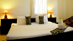 A hotel room with a large bed, two bedside tables with lamps, a window with curtains, and a chair in the corner. - Coconut Grove Bridge House (Elmina)