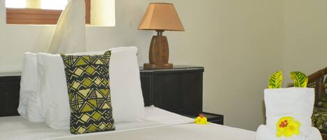 A neatly made bed with white linens, a patterned pillow, and a towel with a flower design.