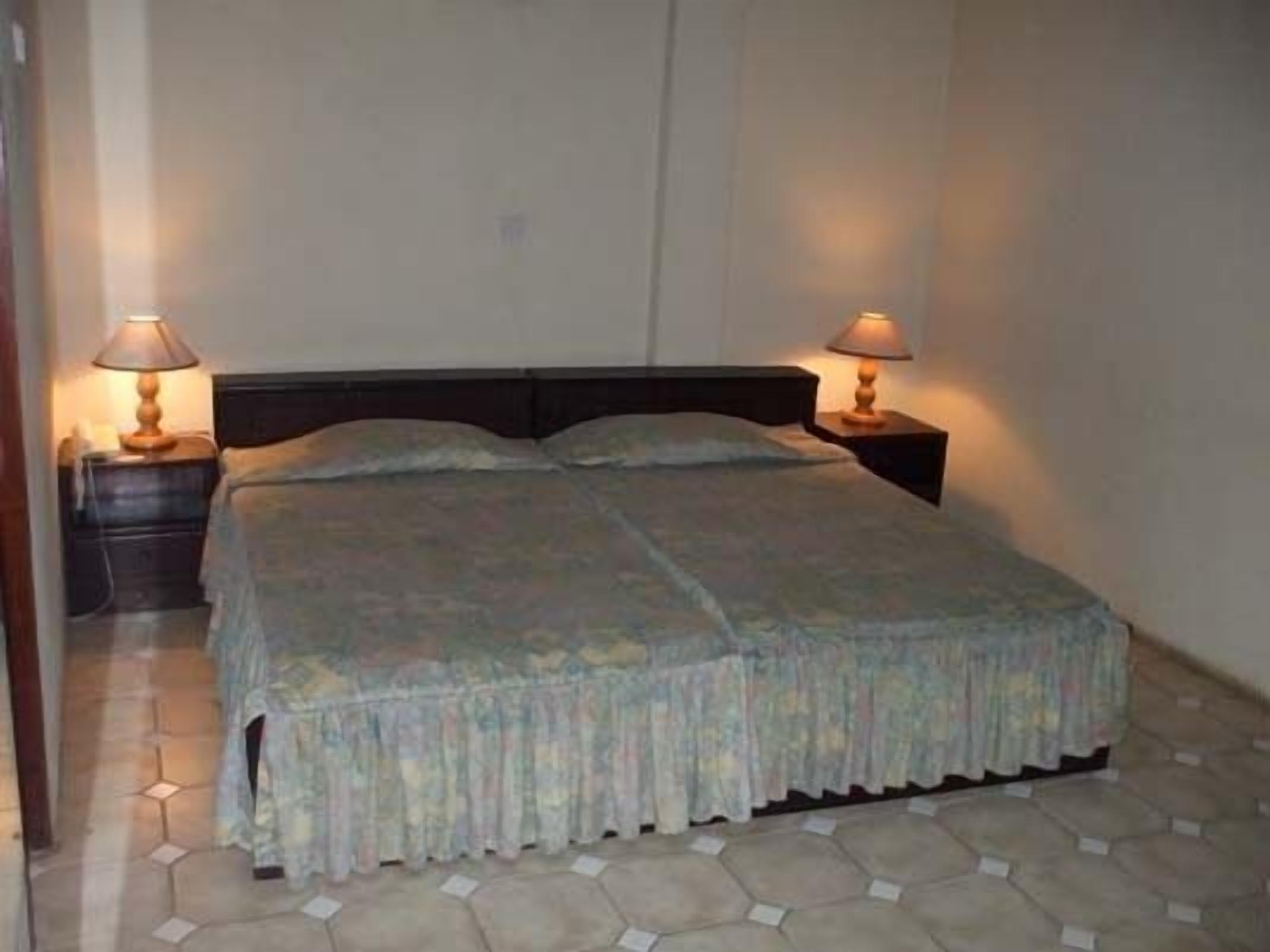 A single bed with a wooden headboard, two bedside tables with lamps, and a patterned bedspread.