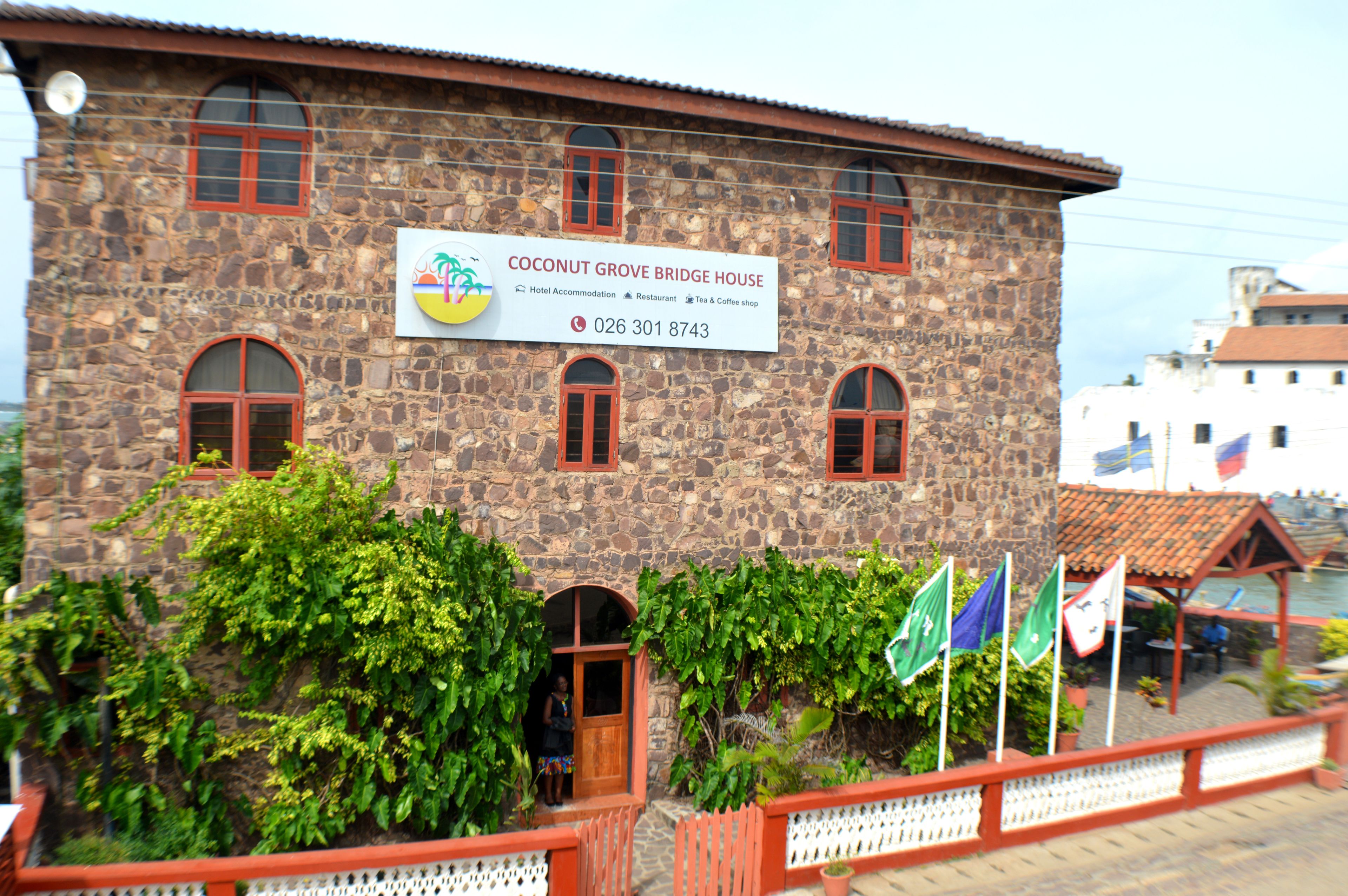 A stone building with a sign for Coconut Grove Bridge House, indicating it offers hotel accommodation, a restaurant, and a tea and coffee shop.