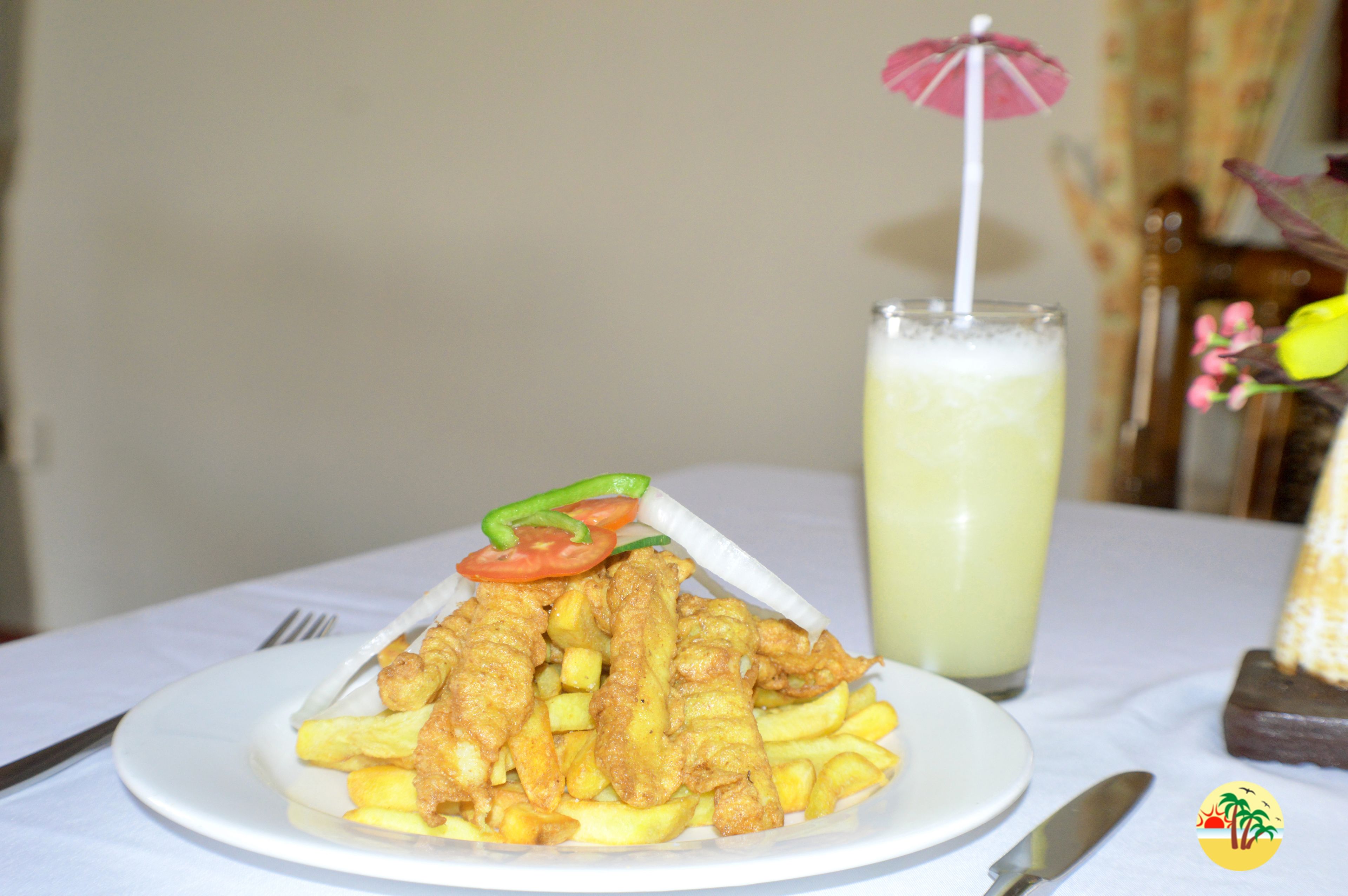 A plate of fried fish and fries with a drink in the background.