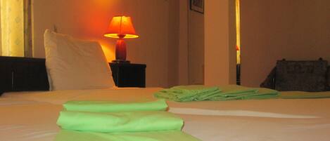 Una habitación de hotel con una cama bien hecha, una lámpara de noche y una puerta que da a otra habitación.