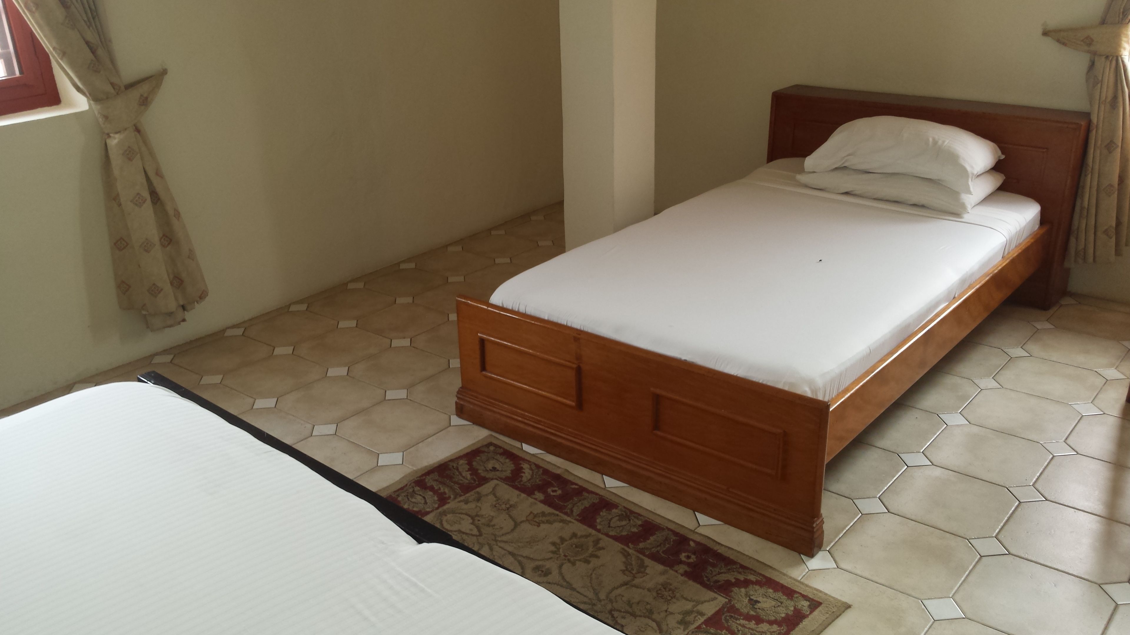 A single bed with a wooden frame and white bedding, a small rug, and hexagonal patterned flooring.