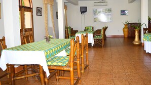 A dining area with wooden chairs and tables, a ceiling fan, and a tiled floor.