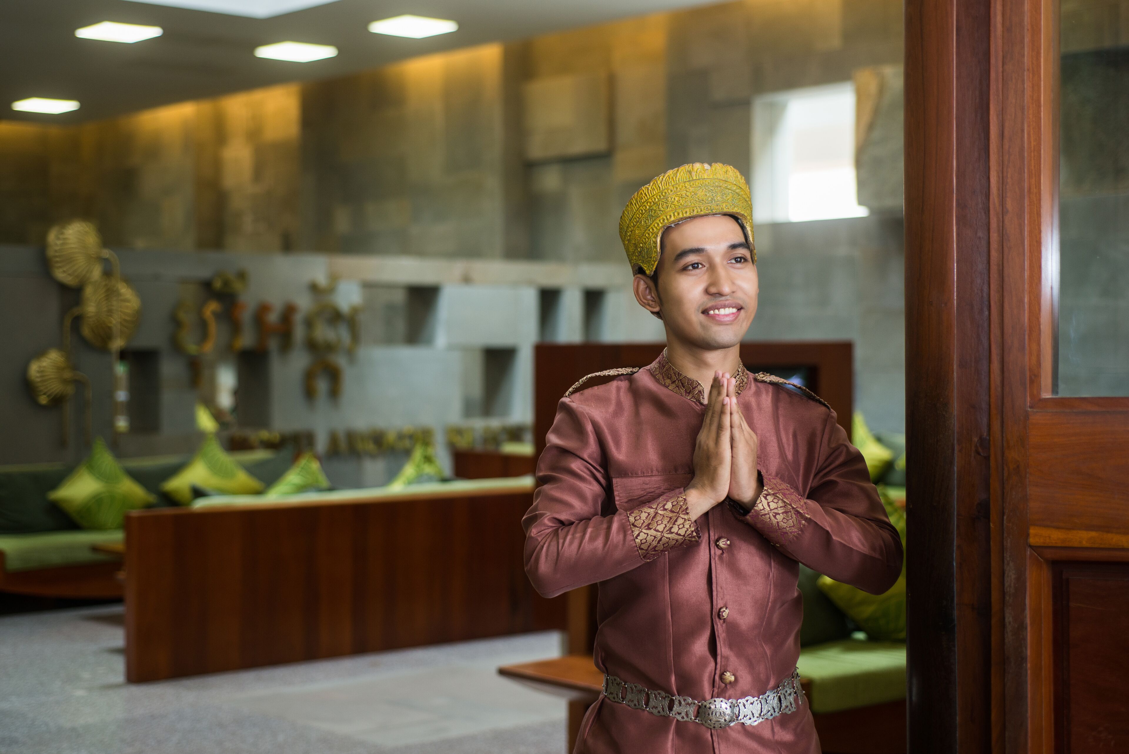 A person in traditional attire standing in a room with a modern interior, including a sofa and decorative wall art.