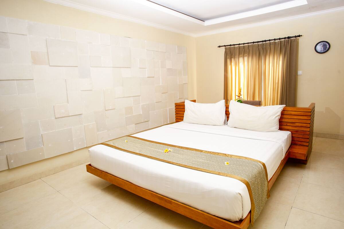 A neatly arranged bedroom with a large bed, a wooden headboard, and a tiled wall.