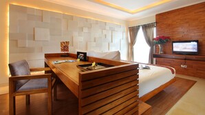 A modern hotel room with a wooden bed, a wooden desk, a TV, and a decorative wall. - Berawa Beach Residence (Tibubeneng)