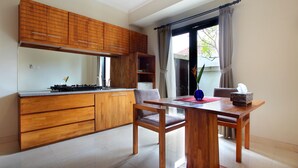 A modern kitchen with wooden cabinets, a dining table with chairs, and a window with curtains. - Berawa Beach Residence (Tibubeneng)