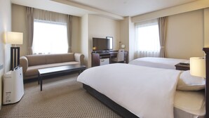 Une chambre d’hôtel avec deux lits, un canapé, un bureau avec une télévision et une lampe.