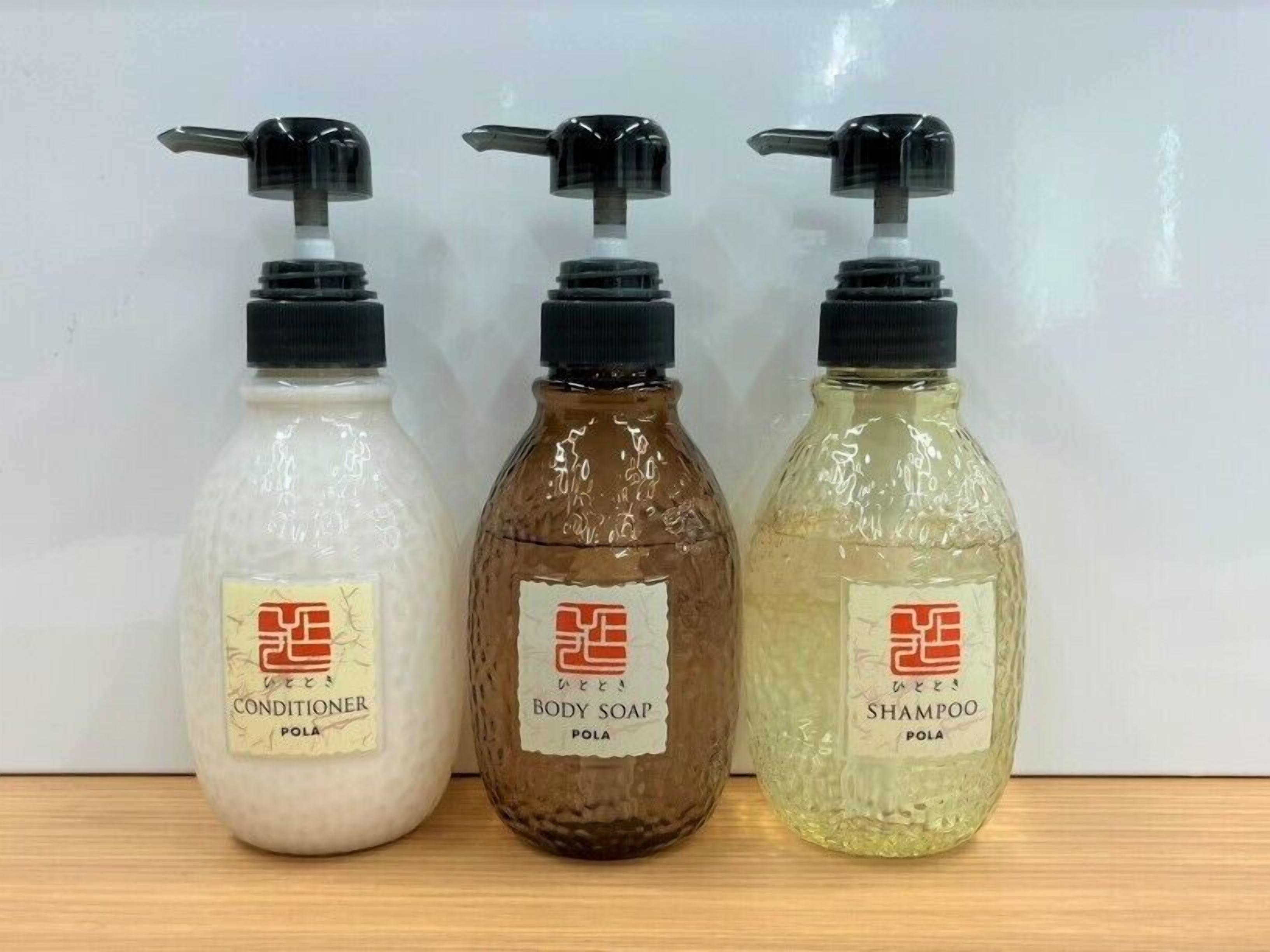 Tres botellas de productos de cuidado personal con dosificadores, etiquetadas como acondicionador, jabón corporal y champú, todas con la marca 'POLA'.