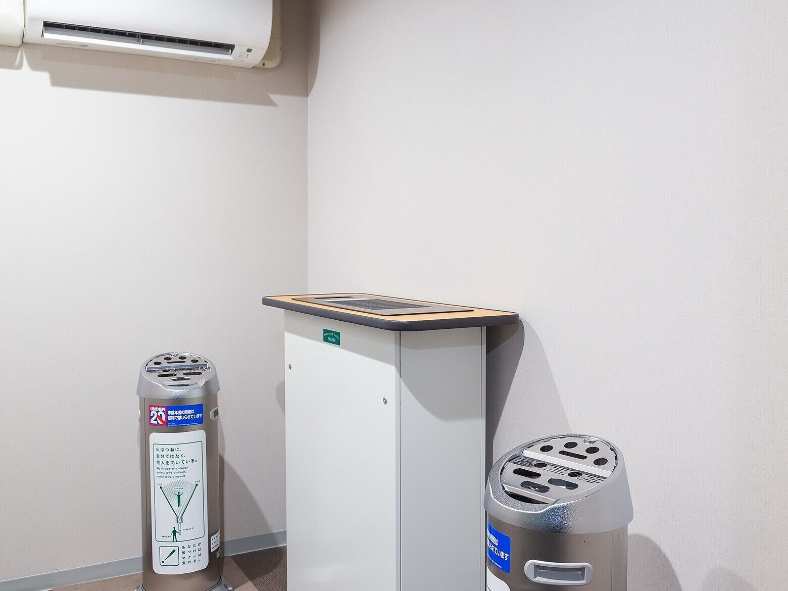 Habitación de hotel con aire acondicionado blanco, un escritorio con una computadora portátil y dos botes de basura.