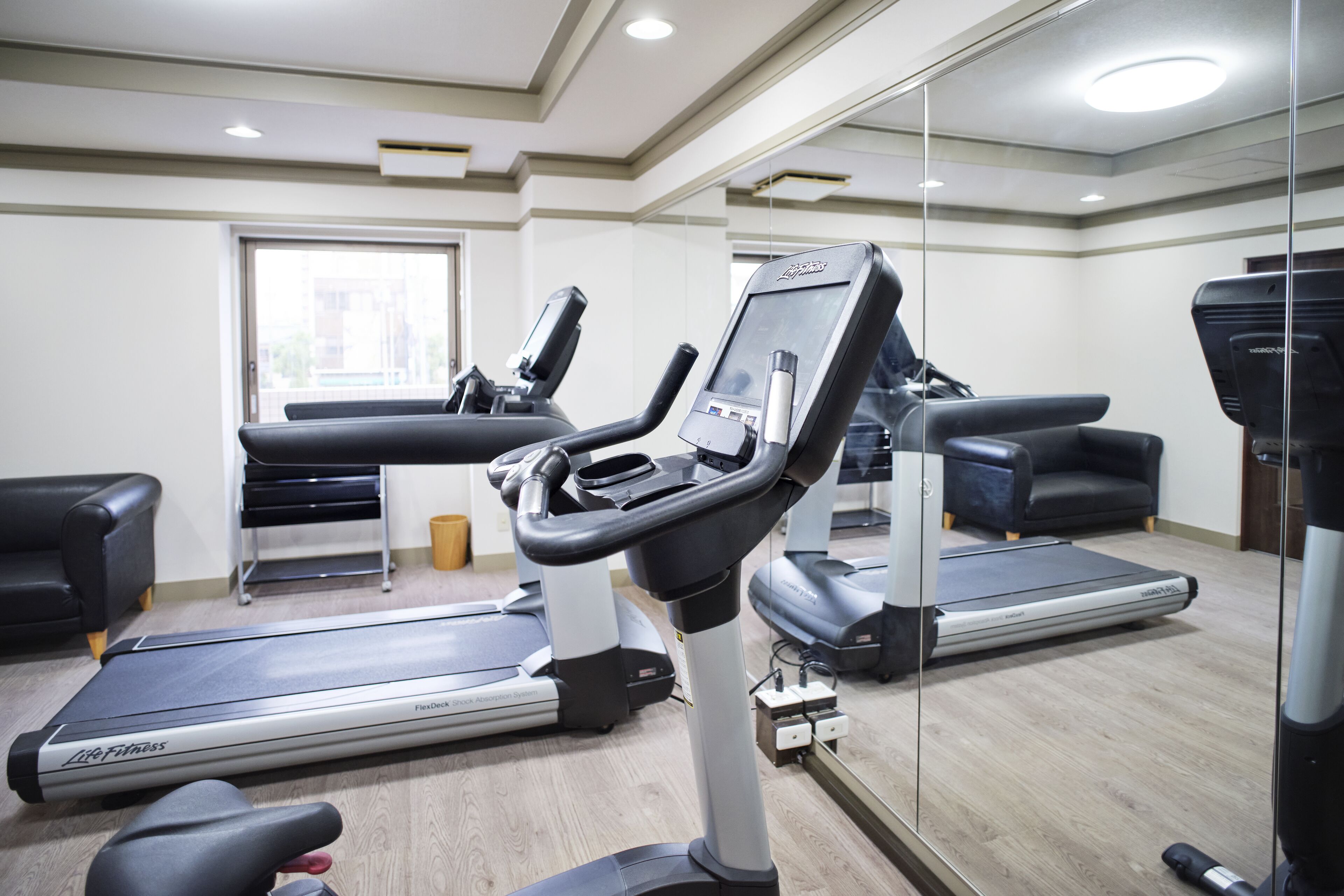 Un gimnasio con cintas de correr, bicicletas estáticas y un espejo grande.