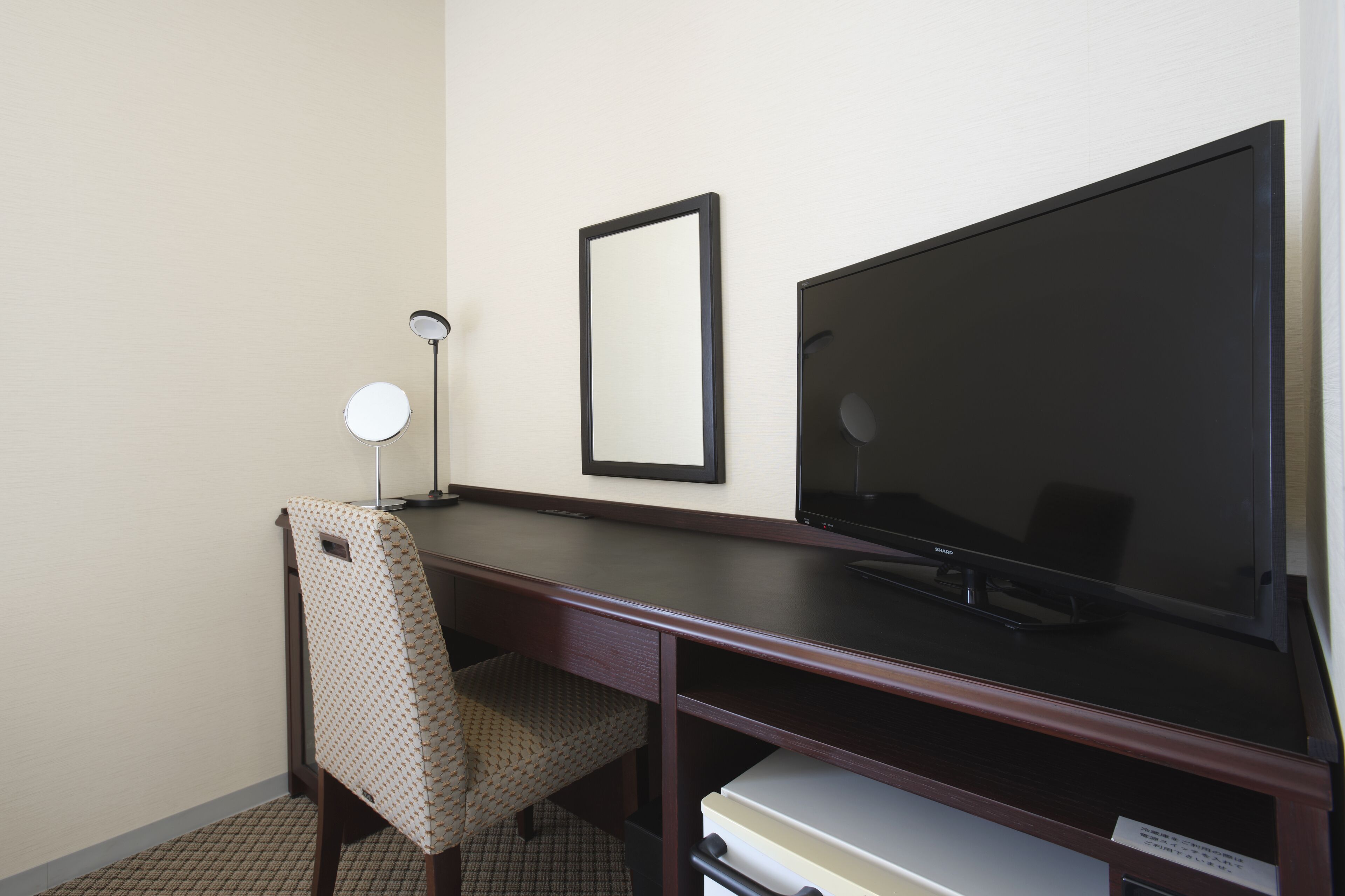 Habitación de hotel con un escritorio de madera oscura, un televisor de pantalla plana, una silla, una lámpara y un cuadro en la pared.