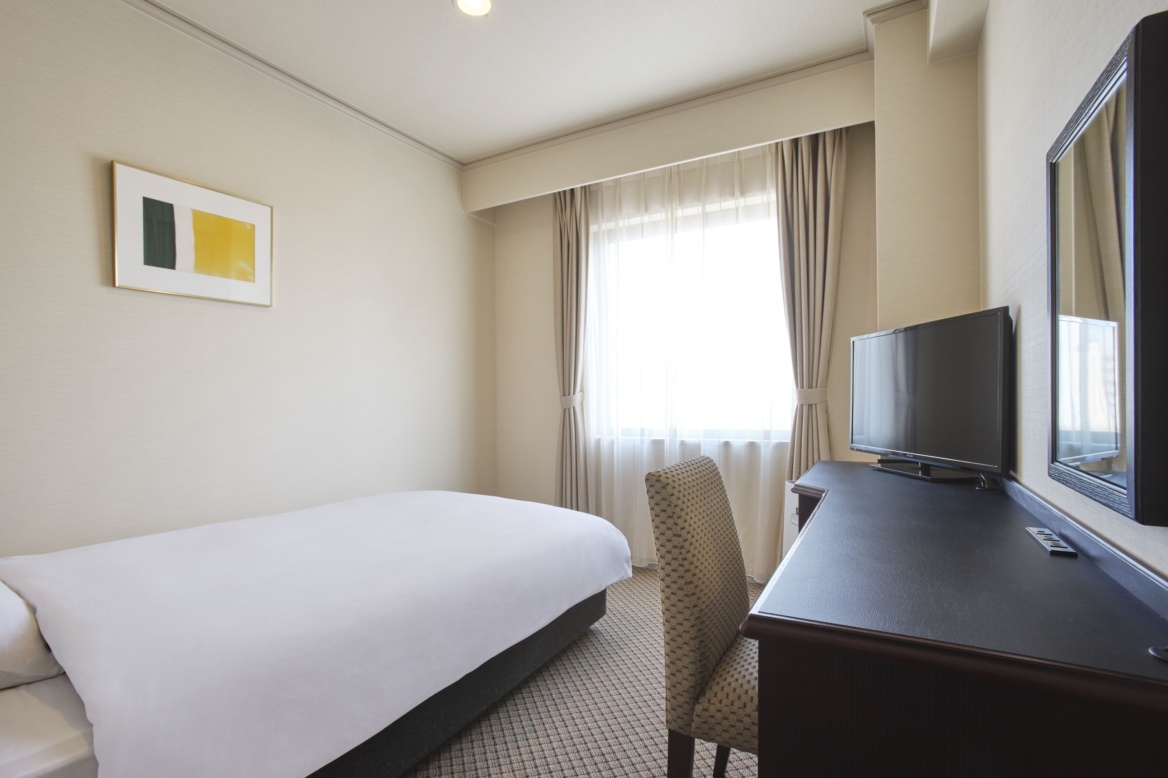 Une chambre d’hôtel avec un lit, un bureau avec une télévision et une chaise.