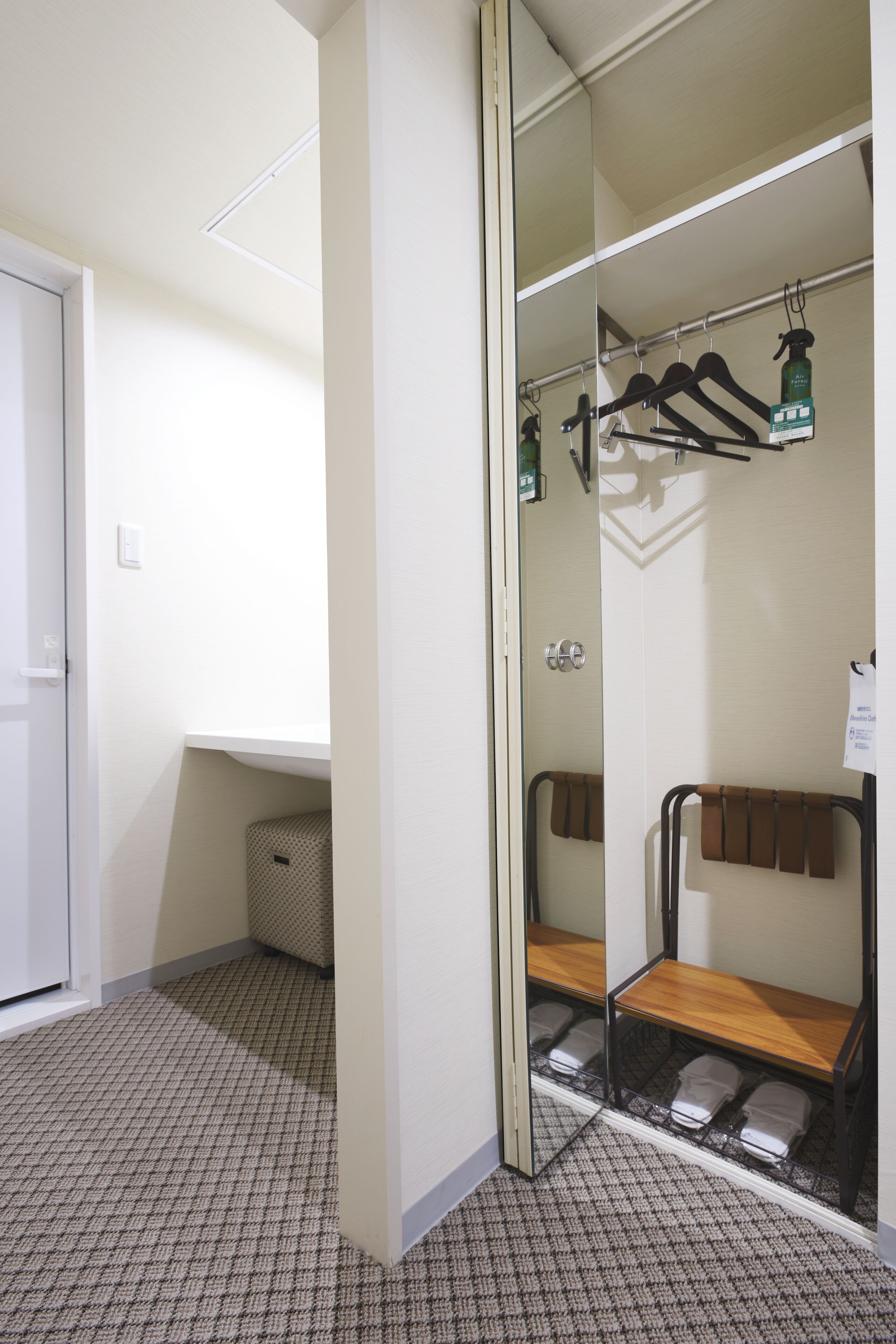 Habitación de hotel con espejo, banca de madera, toallero y un pequeño cesto de basura.