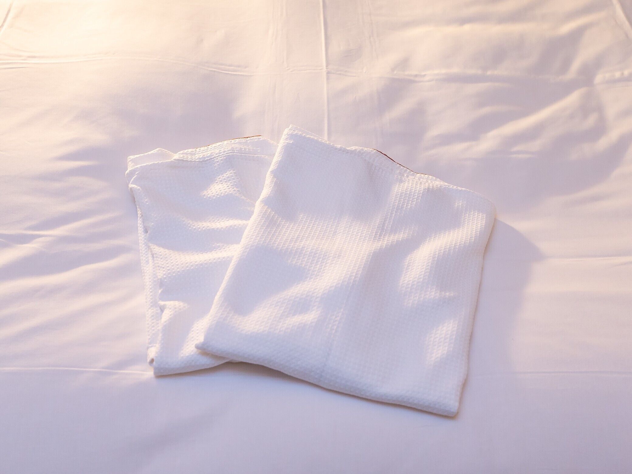 A neatly folded white towel on a bed with a smooth, white sheet.