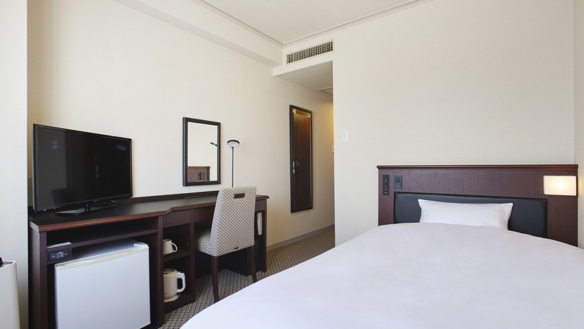Ein Hotelzimmer mit einem Bett, einem Schreibtisch mit Fernseher, einem Sessel, einem Spiegel und einer Tür.