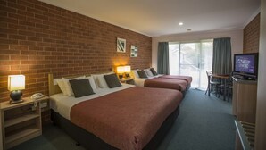 Habitación de hotel con pared de ladrillo, dos camas con ropa de cama roja, un escritorio con televisor y una ventana con cortinas.