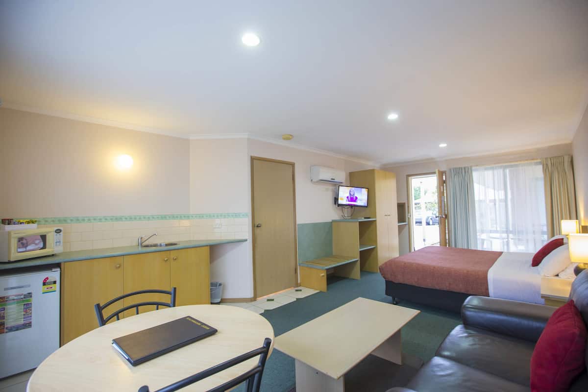 A compact hotel room with a kitchenette, a dining area, a bed, and a seating area.