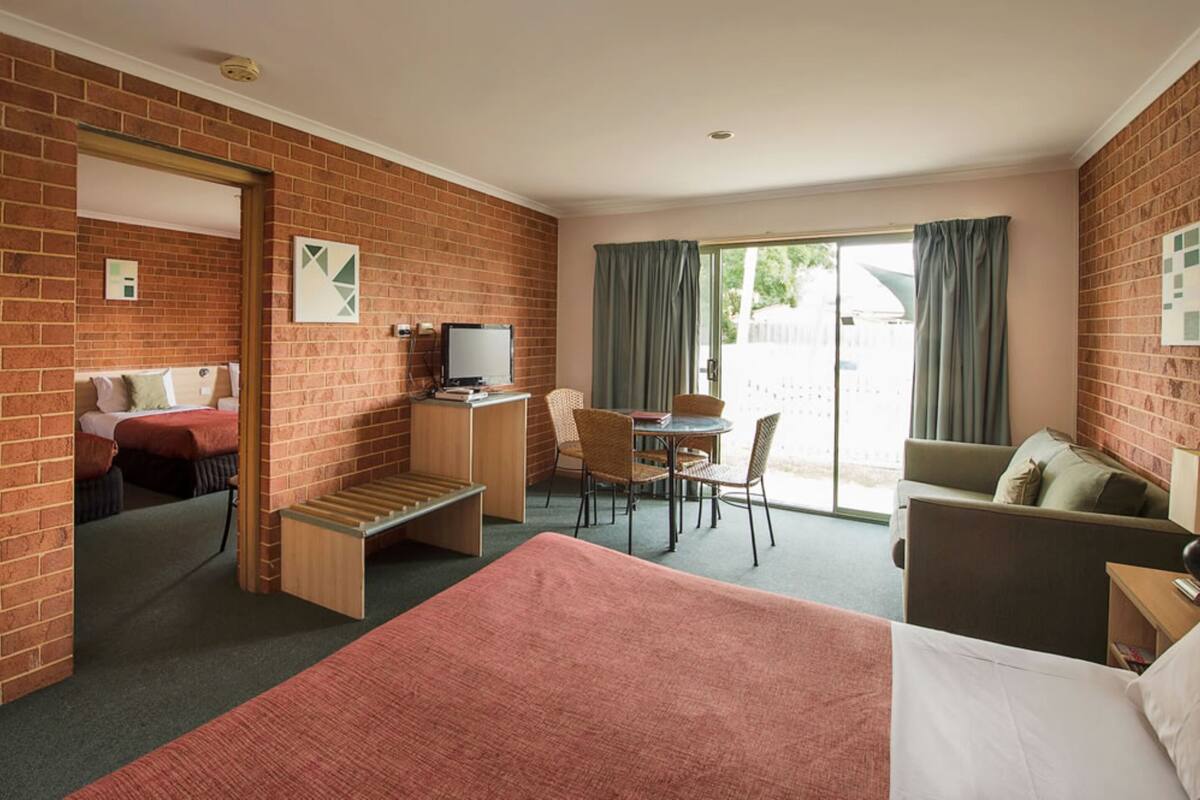 A hotel room with a brick wall, a bed, a desk with a chair, a small table, and a sofa.