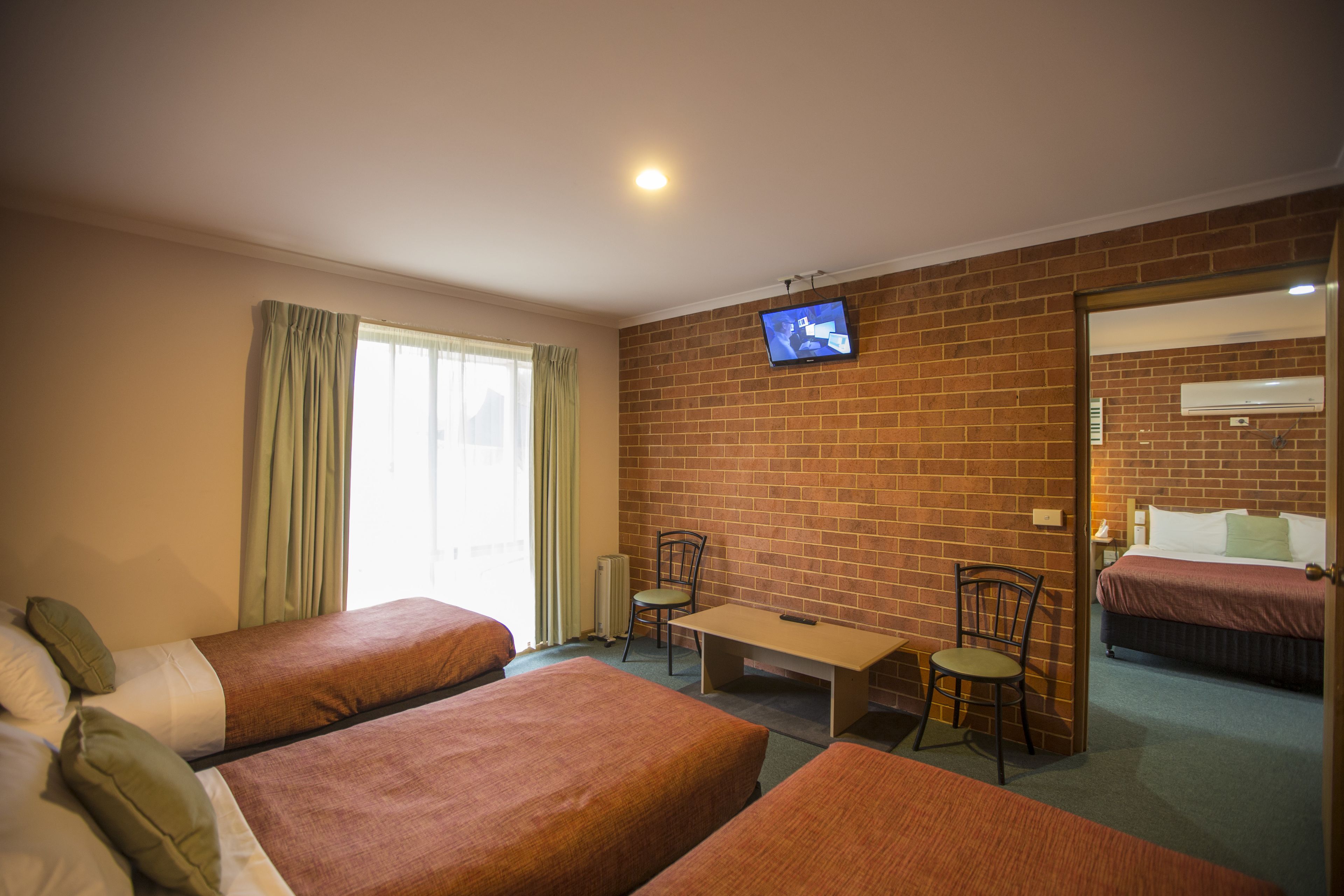 A hotel room with two single beds, a television, a small table, and a chair.