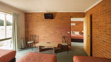 A room with brick walls, a television mounted on the wall, a table with chairs, and two beds.