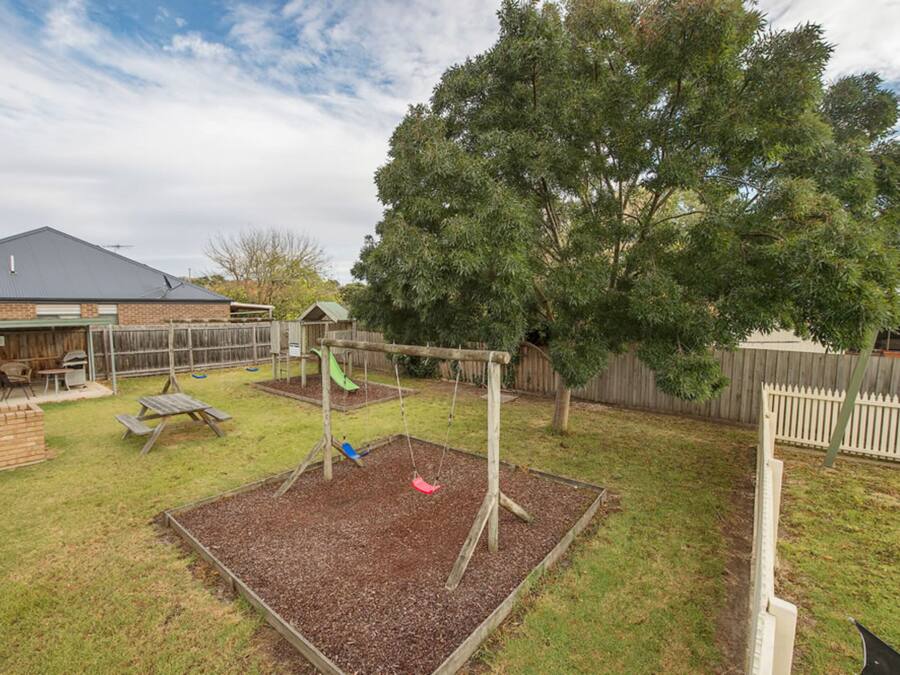 A backyard with a swing set, play area, and a large tree.
