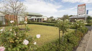 Un motel con césped verde, un jardín de rosas y una zona de estacionamiento techada.