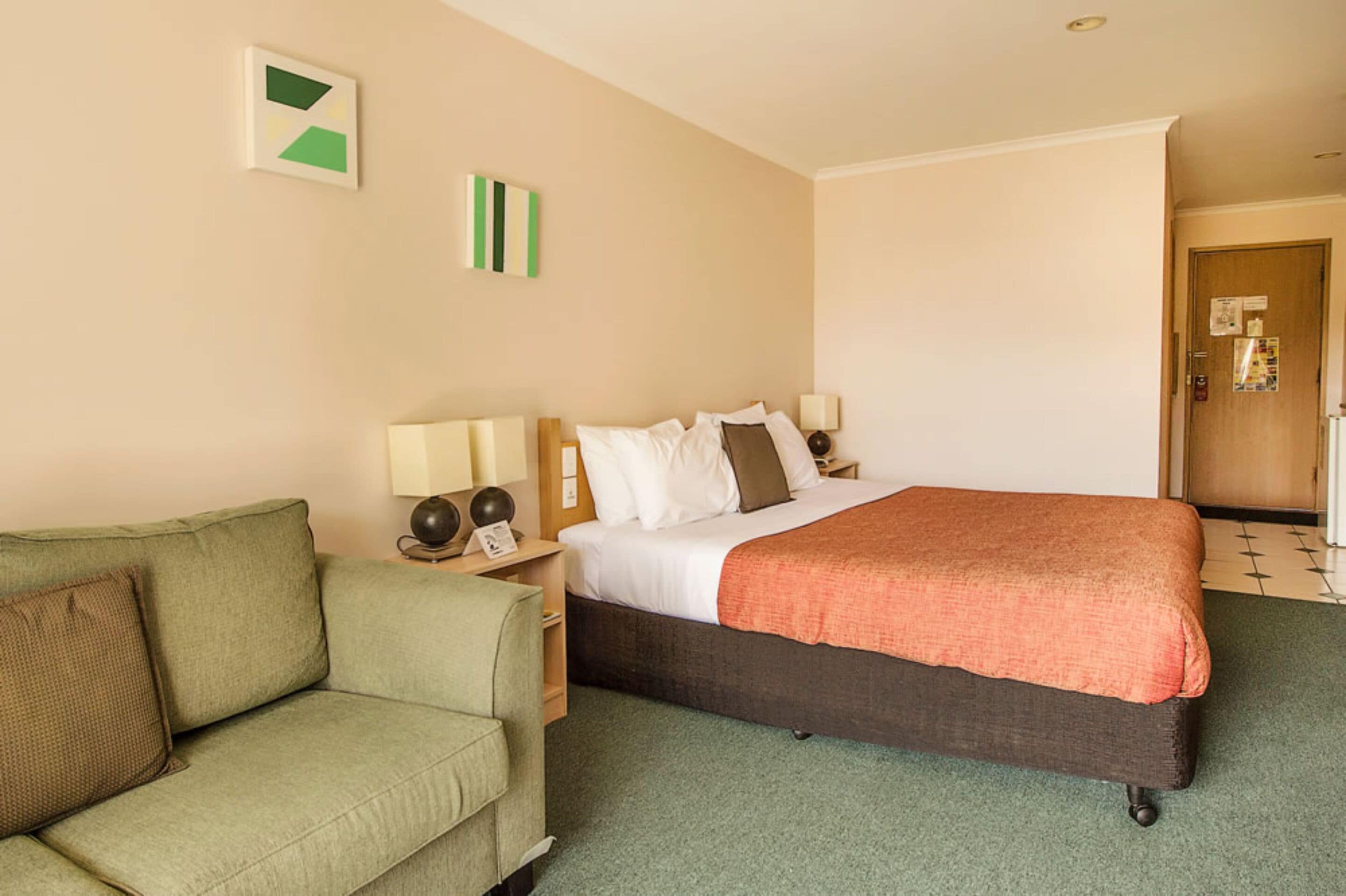A hotel room with a bed, a green sofa, and a nightstand with a lamp.