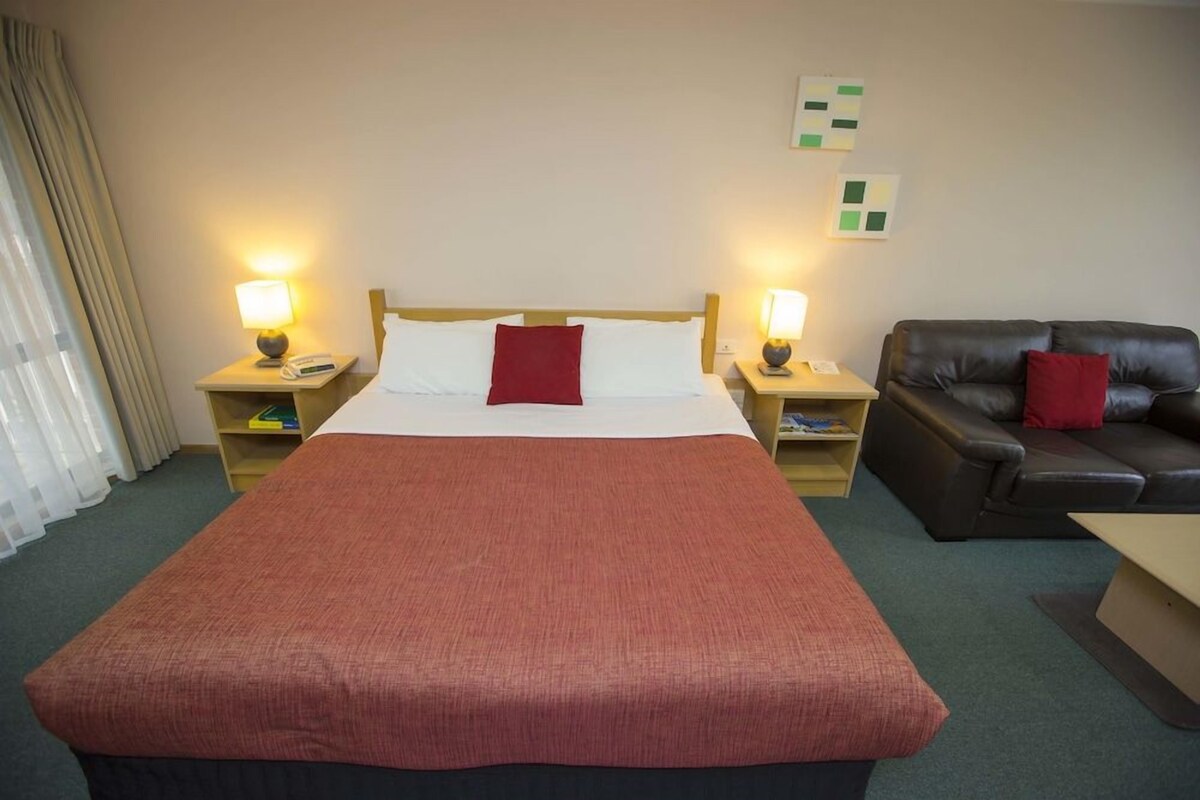 A hotel room with a large bed, two bedside tables with lamps, a leather sofa, and a small table.