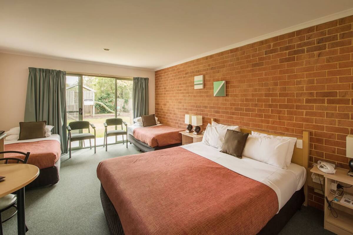 A hotel room with two beds, a desk, and a chair. There is a brick wall and a window with curtains.
