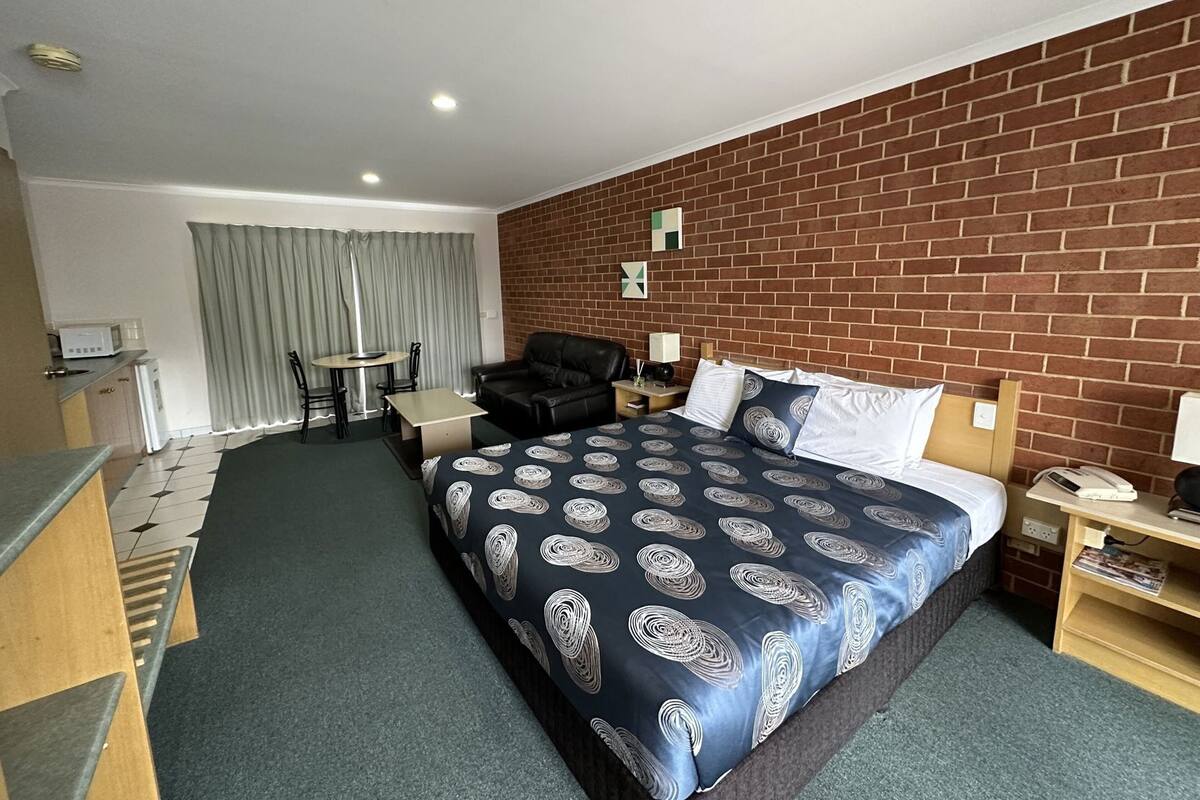 A hotel room with a bed, a desk, a chair, a table, and a brick wall.