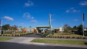 A commercial building with a green roof, a parking lot, and a clear blue sky.