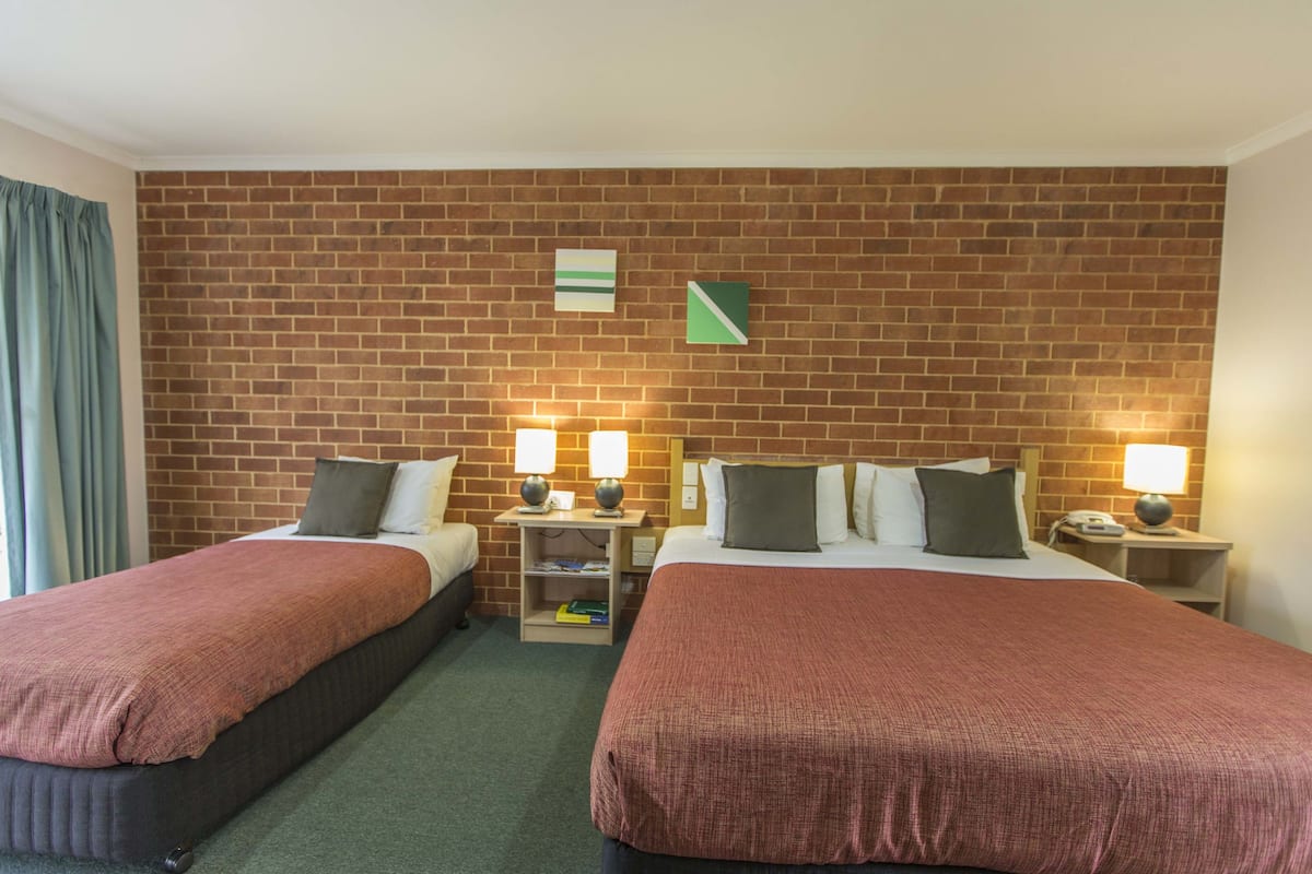 A hotel room with two beds, a brick wall, and a green curtain.